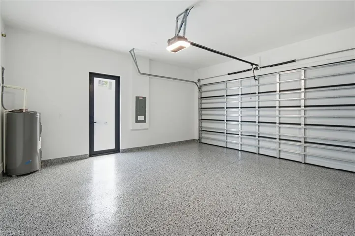 Garage featuring electric water heater, electric panel, and a garage door opener
