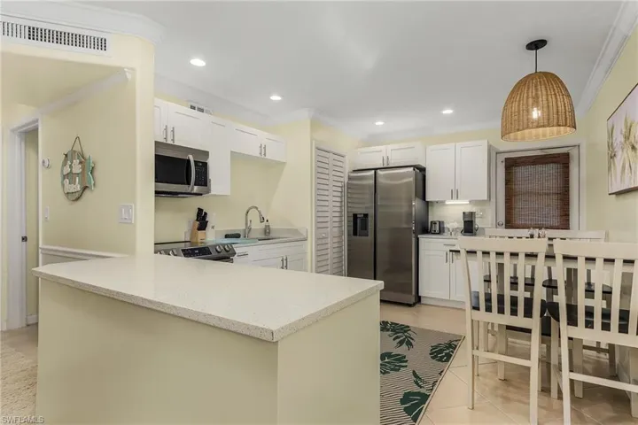 Kitchen featuring ornamental molding, stainless steel appliances, light stone countertops, a peninsula, and white cabinetry
