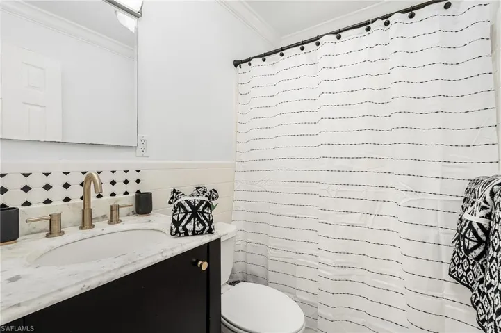Bathroom with ornamental molding, vanity, curtained shower, and tile walls