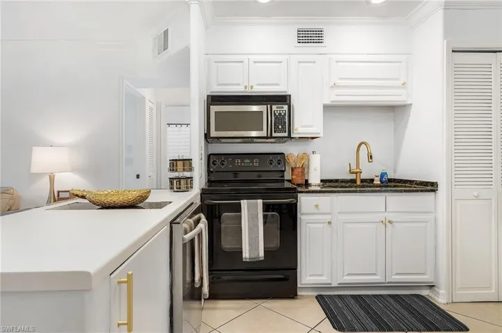 Kitchen with black range with electric cooktop, white cabinets, a peninsula, ornamental molding, and stainless steel microwave