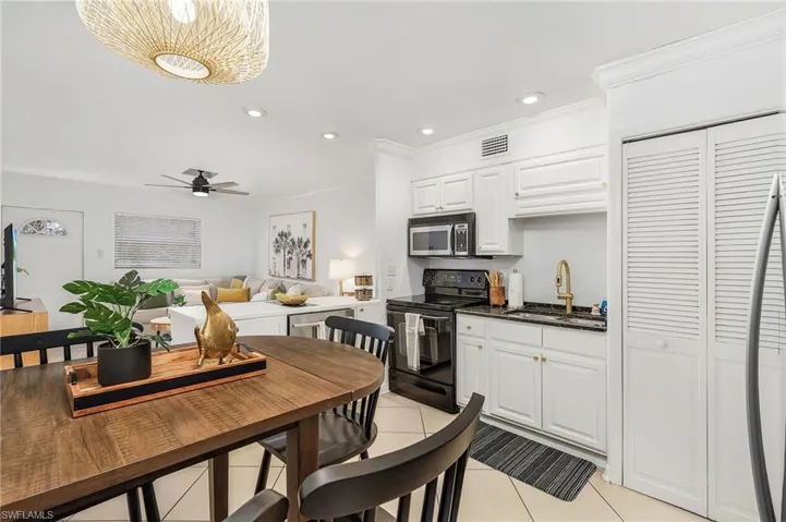 Kitchen with black electric range, recessed lighting, white cabinetry, light tile patterned floors, and stainless steel microwave