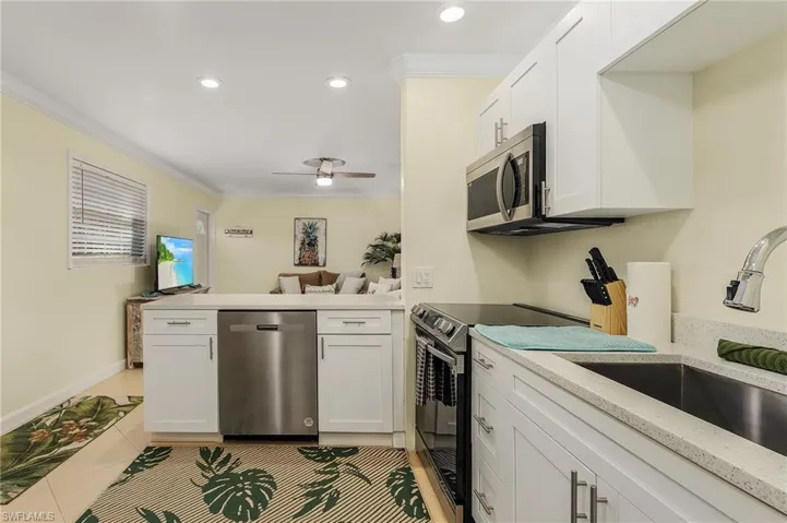 Kitchen with a peninsula, stainless steel appliances, crown molding, white cabinets, and light tile patterned floors