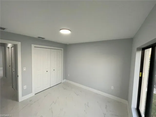 Unfurnished bedroom featuring multiple windows, light marble finish floors, and a closet