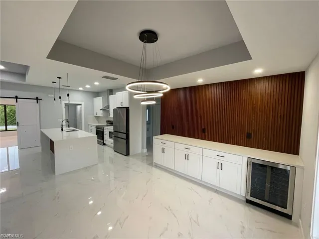 Kitchen featuring a barn door, a large island with sink, light marble finish floors, beverage cooler, and appliances with stainless steel finishes