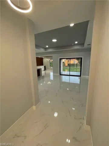 Corridor featuring marble finish flooring, recessed lighting, and a tray ceiling