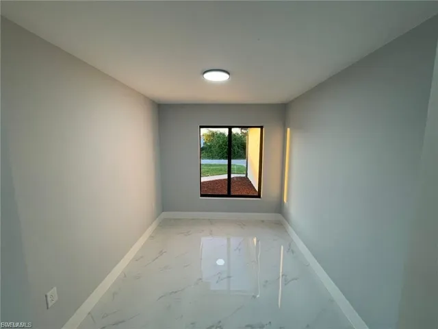 Unfurnished room featuring light marble finish flooring and baseboards