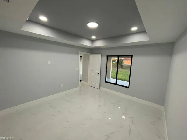 Unfurnished room with a tray ceiling, recessed lighting, and light marble finish floors