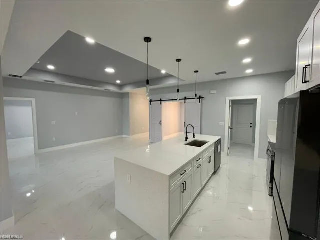 Kitchen with a barn door, light marble finish flooring, recessed lighting, freestanding refrigerator, and a kitchen island with sink