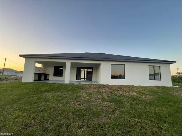Back of house at dusk featuring stucco siding, a yard, and a patio