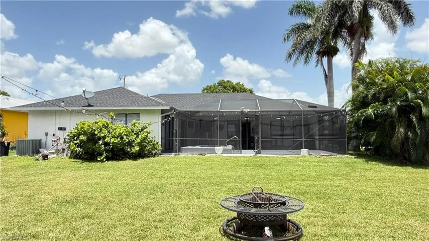 Back of house with stucco siding, a yard, an outdoor fire pit, a lanai, and a shingled roof