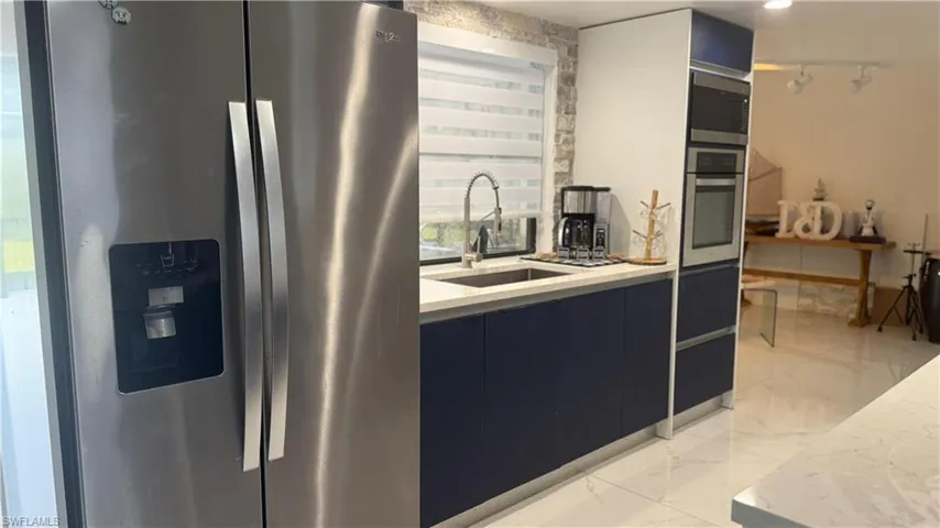 Kitchen with stainless steel appliances, modern cabinets, rail lighting, light marble finish floors, and dark cabinetry