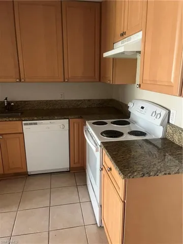 Kitchen featuring range hood, light tile patterned floors, sink, dishwashing machine, and white stove