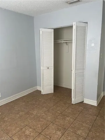 Unfurnished bedroom featuring dark tile patterned flooring, a textured ceiling, and a closet