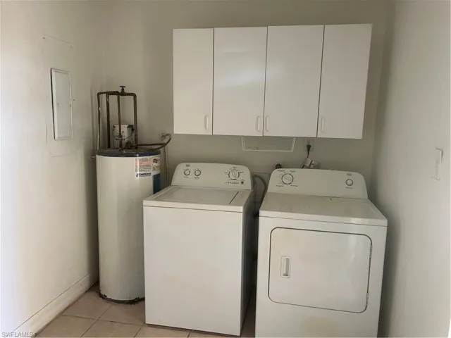 Laundry room featuring electric panel, cabinets, water heater, light tile patterned floors, and washing machine and dryer