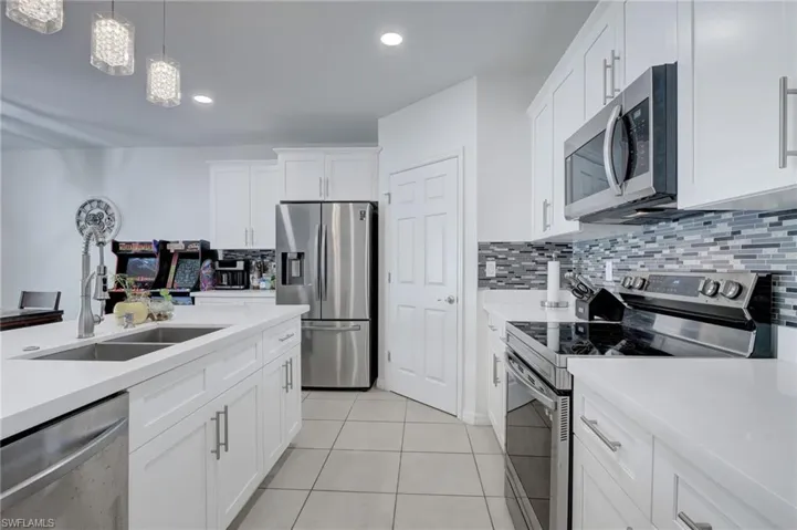 Kitchen featuring stainless steel appliances, white cabinets, backsplash, hanging light fixtures, and light tile patterned flooring