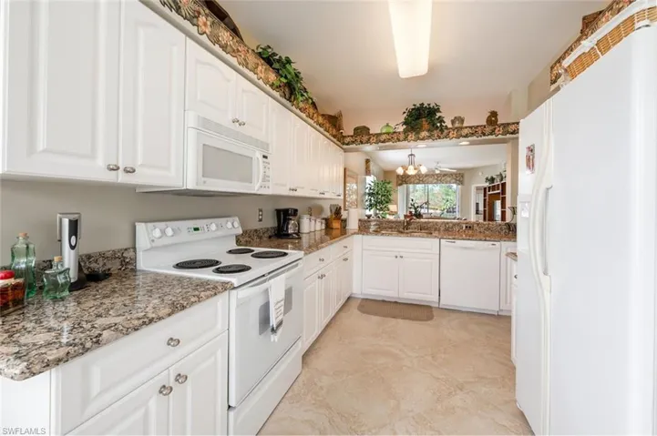 Kitchen with white appliances, light stone countertops, sink, white cabinets, and a chandelier