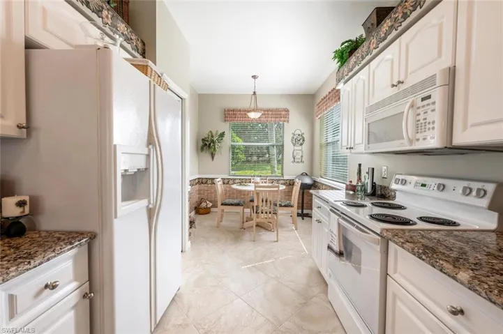 Kitchen featuring white appliances, dark stone countertops, white cabinetry, and hanging light fixtures