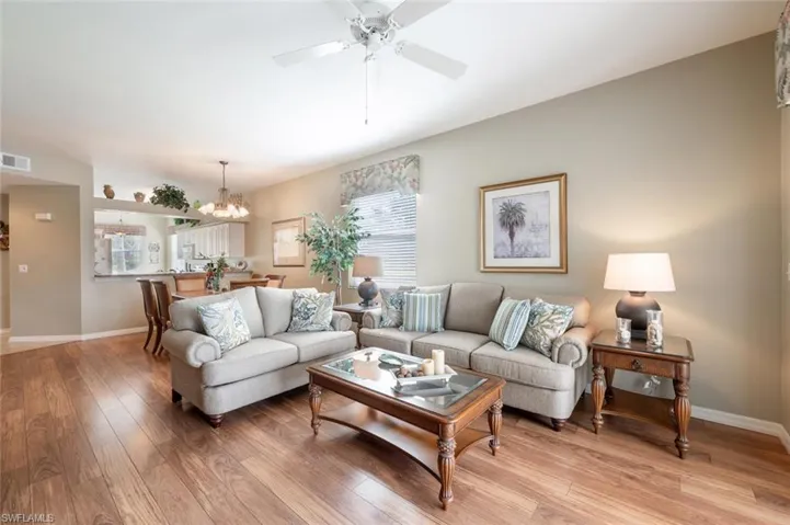 Living room with light hardwood / wood-style flooring, ceiling fan with notable chandelier, and a wealth of natural light