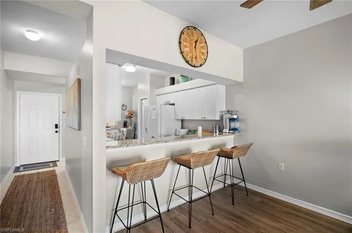 Kitchen featuring a kitchen bar, white cabinets, white refrigerator with ice dispenser, dark wood-style flooring, and a peninsula