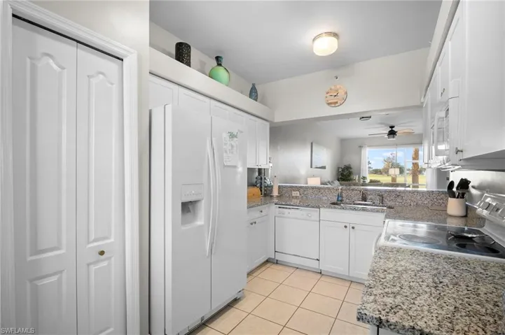Kitchen featuring white appliances, white cabinets, light tile patterned floors, and light stone countertops