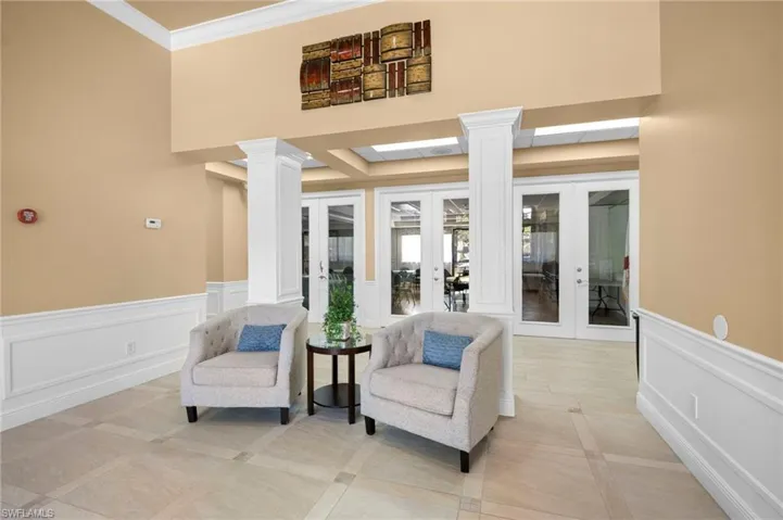 Living area with a wainscoted wall, a decorative wall, ornate columns, crown molding, and inlaid floor details