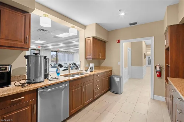 Kitchen featuring a wainscoted wall, dishwasher, light stone countertops, brown cabinets, and a decorative wall