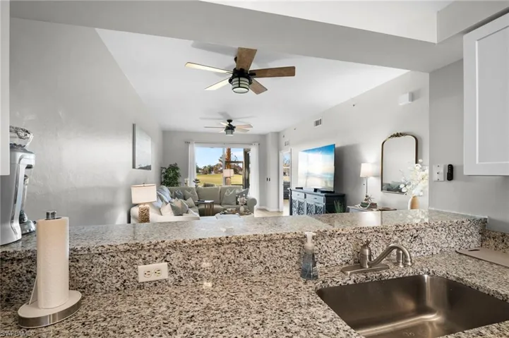 Kitchen with light stone countertops, open floor plan, white cabinetry, and ceiling fan