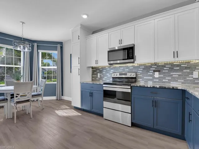 Kitchen featuring blue cabinets, appliances with stainless steel finishes, white cabinets, decorative backsplash, and decorative light fixtures