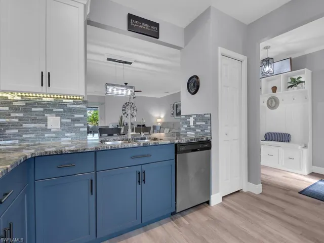 Kitchen featuring blue cabinets, backsplash, dark stone counters, stainless steel dishwasher, and pendant lighting
