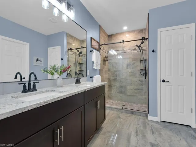 Full bath with a stall shower, double vanity, and light marble finish floors