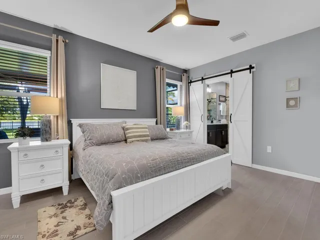 Bedroom featuring a barn door, light wood-style flooring, ensuite bath, and ceiling fan