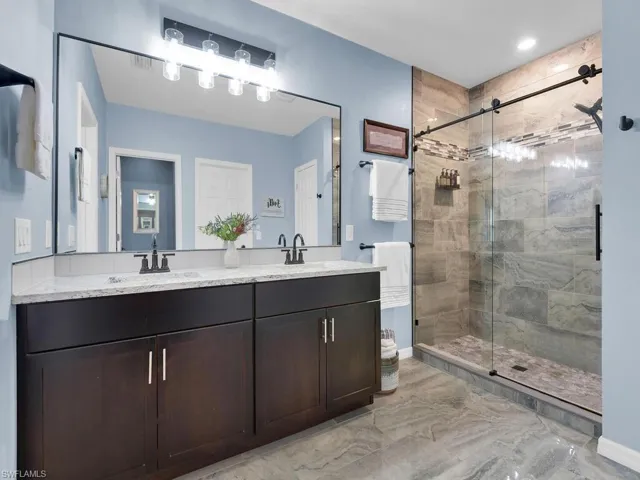 Bathroom featuring a shower stall, double vanity, and light marble finish flooring