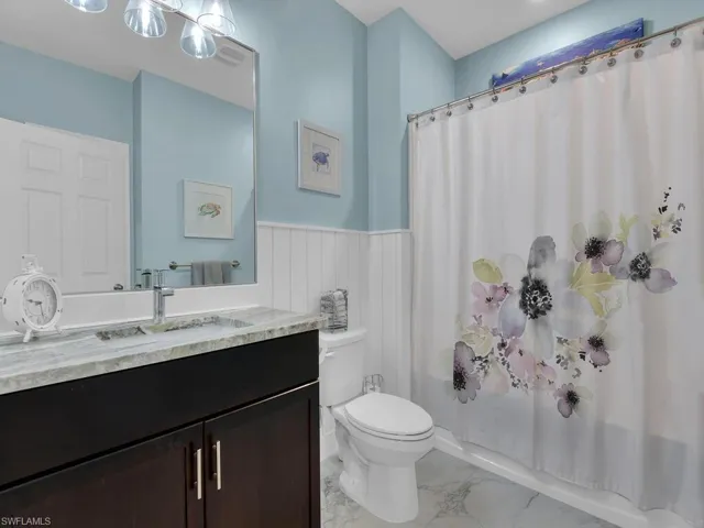 Full bath featuring shower / bathtub combination with curtain, vanity, light marble finish flooring, and a wainscoted wall