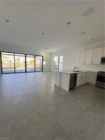 Kitchen with white cabinetry, range, dishwashing machine, open floor plan, and light tile patterned floors