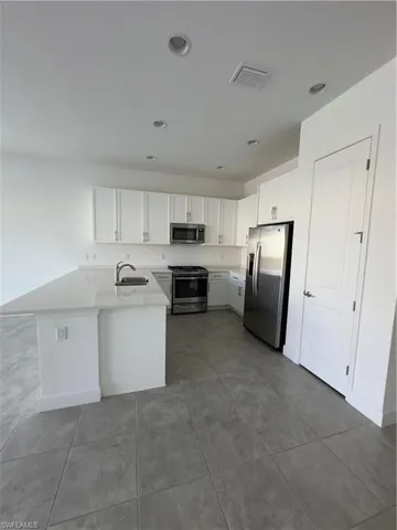 Kitchen featuring white cabinetry, appliances with stainless steel finishes, a peninsula, light stone counters, and recessed lighting