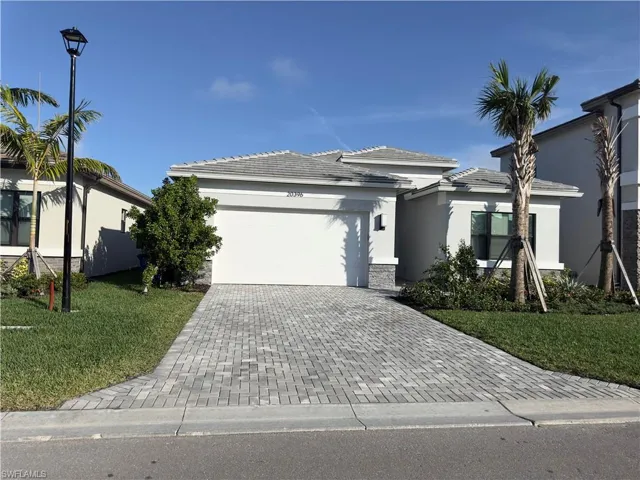 View of front of property featuring stucco siding, decorative driveway, stone siding, a front lawn, and an attached garage