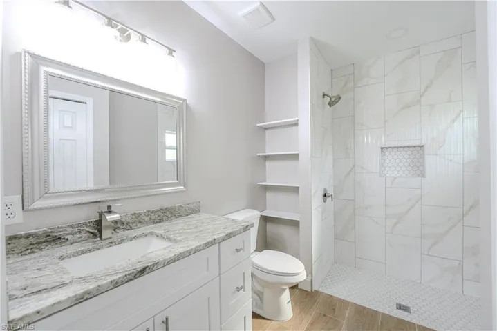 Full bathroom featuring vanity, toilet, a tile shower, visible vents, and wood finished floors