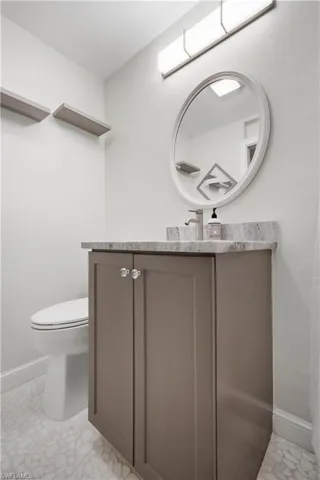 Vanity featuring a stone countertop, an oval mirror with a white frame, and a wall-mounted light fixture