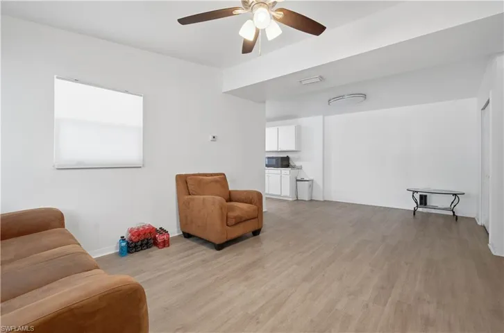 Open-concept living area featuring wood-finish flooring, a ceiling fan with integrated lighting, and a window with a roller shade