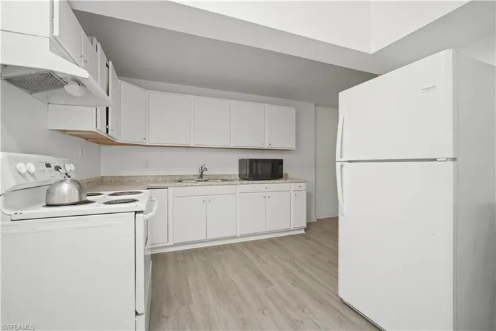 Kitchen featuring light wood-finish flooring, white cabinetry, a white electric range with a range hood, and a white refrigerator