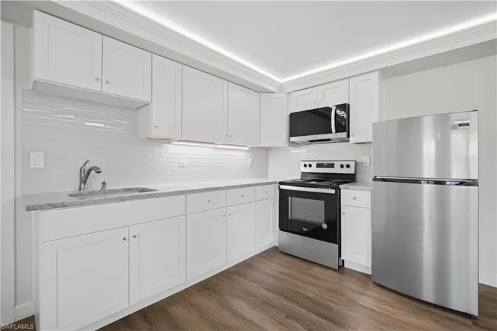 Kitchen featuring white shaker-style cabinetry, light-toned countertops, a glass subway tile backsplash, stainless steel appliances, and wood-finish flooring