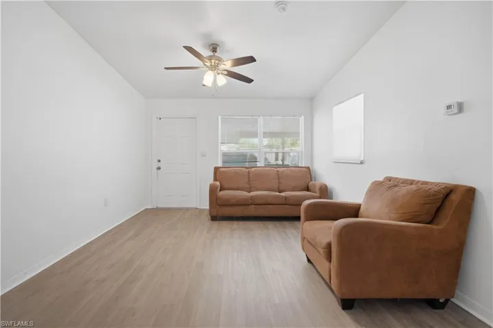 Open living space featuring wood-finish flooring, a ceiling fan with integrated lighting, and multiple windows with horizontal blinds