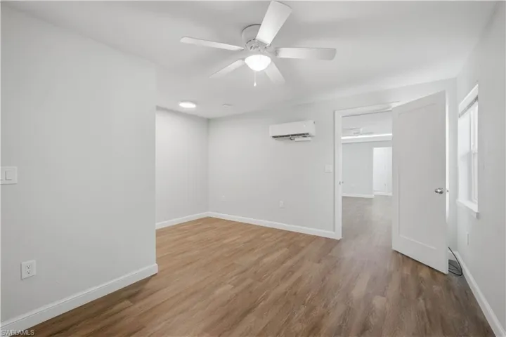Spacious room featuring wood-finish flooring, a ceiling fan with integrated lighting, a wall-mounted mini-split system, recessed lighting, and a white interior door