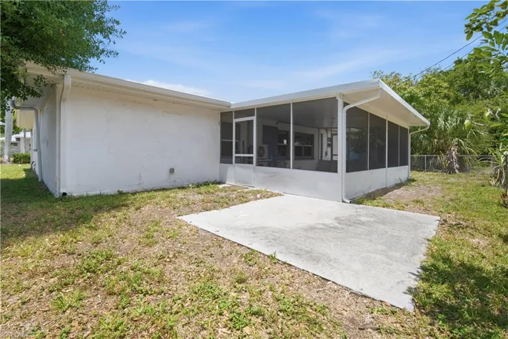 Rear exterior featuring a screened-in porch, white stucco siding, and a concrete patio pad