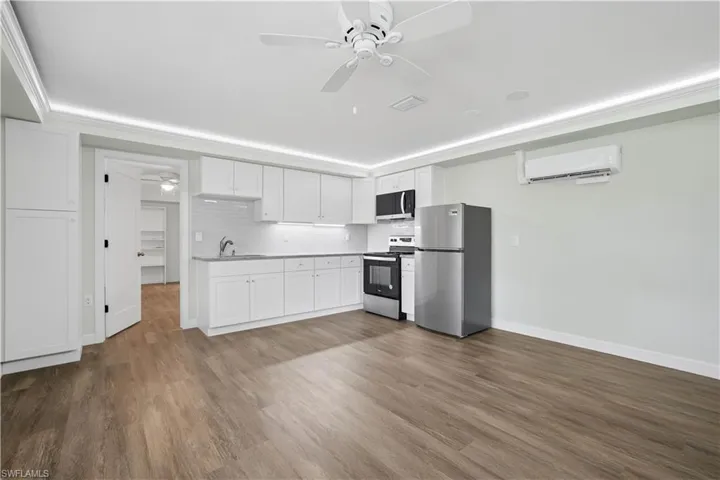 Contemporary kitchen area with wood-finish flooring, white cabinetry, light countertops, and a white subway tile backsplash