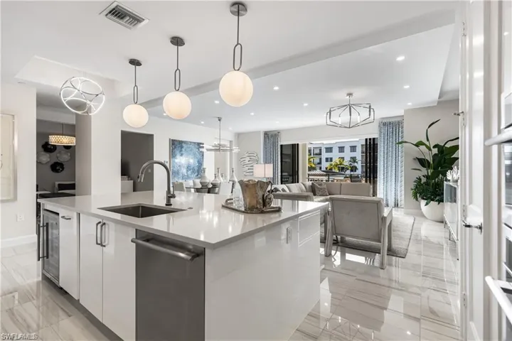 Kitchen with pendant lighting, an inviting chandelier, white cabinets, sink, and a large island