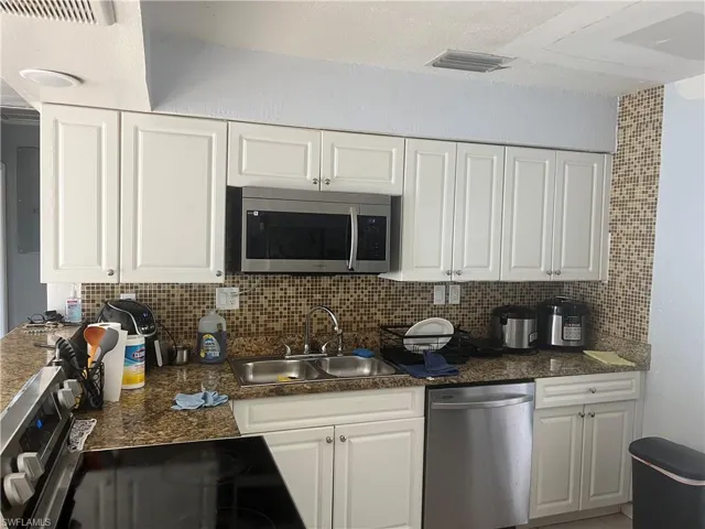 Kitchen with stainless steel appliances, white cabinetry, backsplash, and dark stone countertops