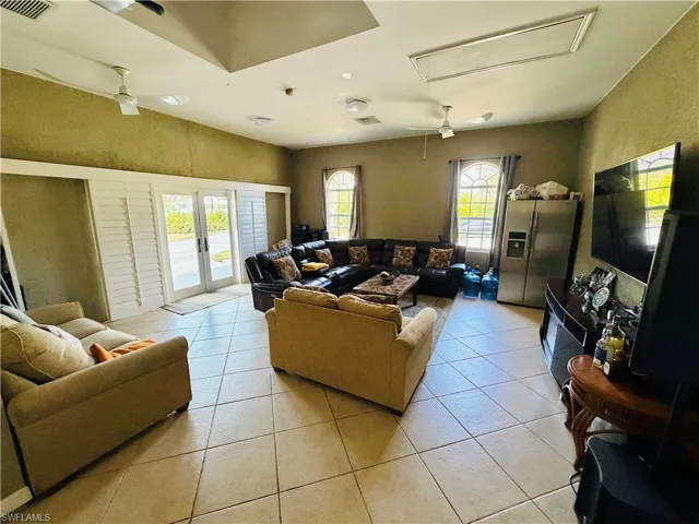 Living area with ceiling fan, french doors, plenty of natural light, light tile patterned floors, and a textured wall