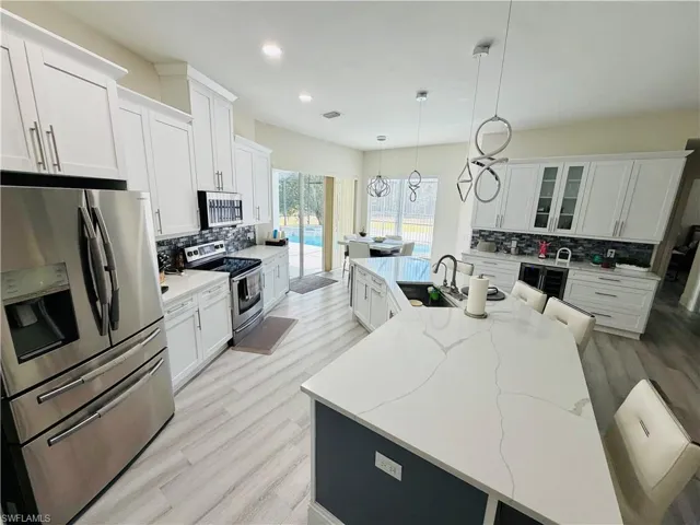 Kitchen with stainless steel appliances, white cabinets, a center island with sink, and light wood-style floors