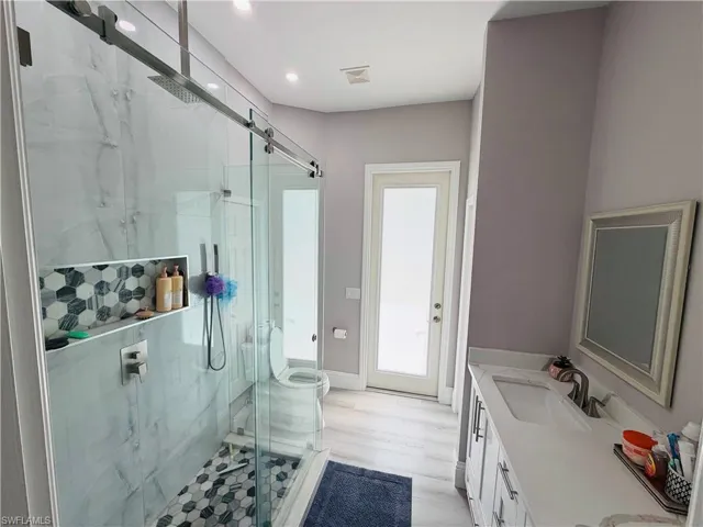 Full bath with double vanity, a marble finish shower, and light wood-style flooring